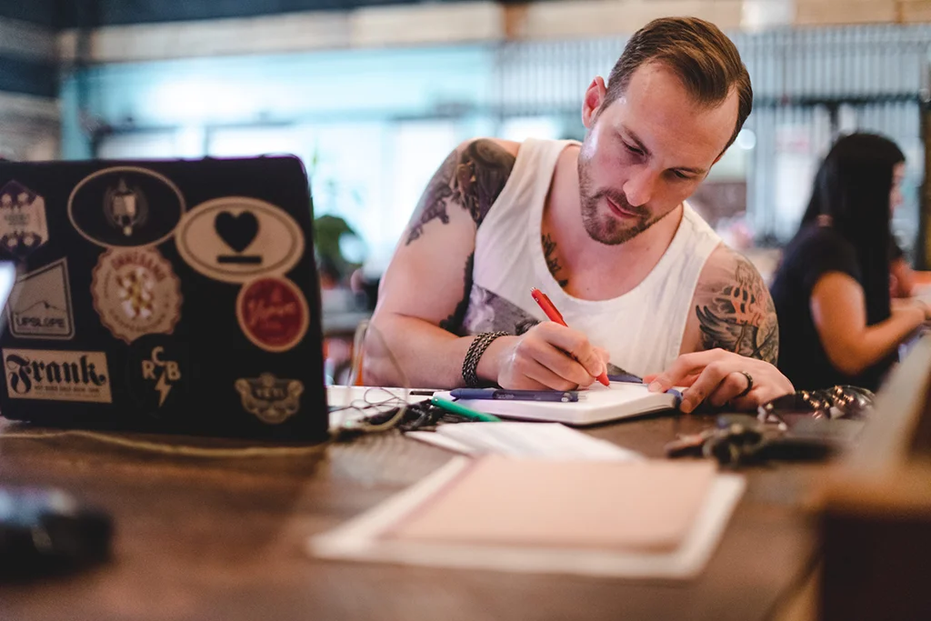 man with tatoos writing in a coworking office