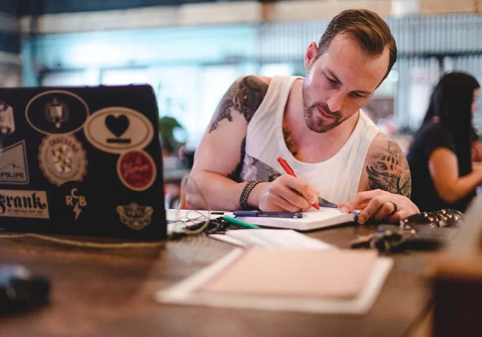 man with tatoos writing in a coworking office